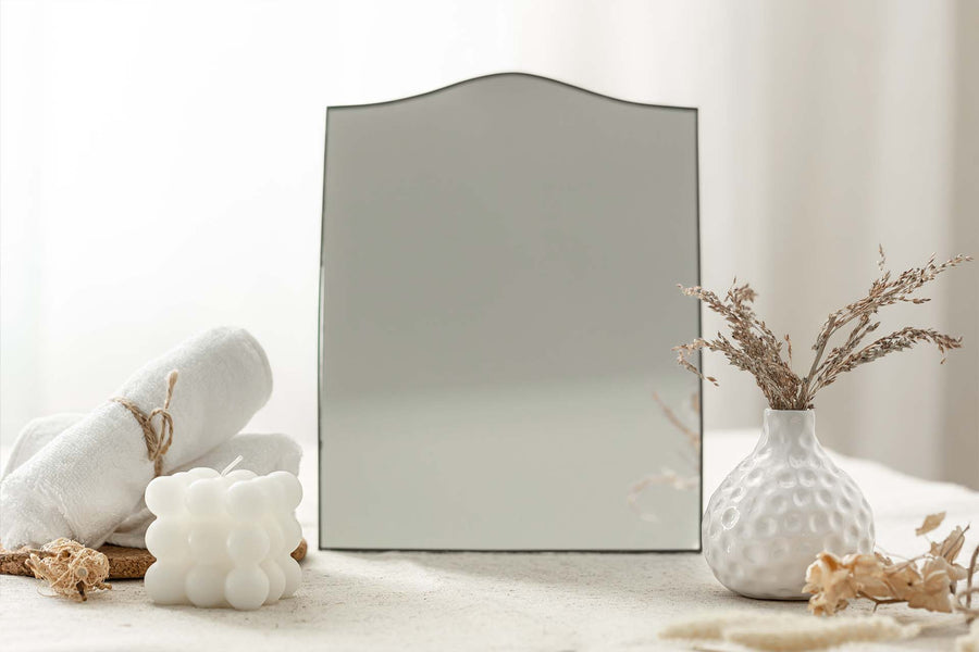 white arch mirror with curved top placed on neutral styled table with decor elements